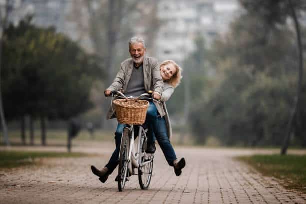 Happy mature couple having fun on a bicycle in autumn day at the park.