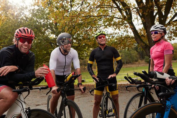 A group of cyclists stop to chat and laugh on a small country lane.