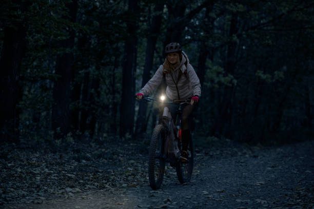 Low-key photo of a cheerful young woman riding her enduro mountain bike (eMTB) at night, with a front light on.