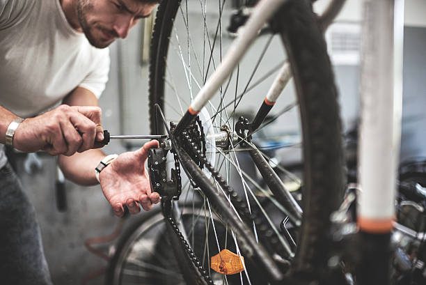 Male mechanic inside bicycle store repairing the transmission mechanism on mountain bike.