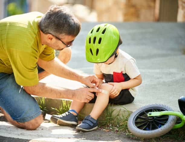 Shot of a father applying antibacterial medical bandage on child's knee after falling down from a cycle