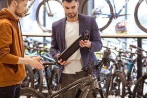 Salesman and young businessman watching e-bikes in bike shop. Customer holding battery.