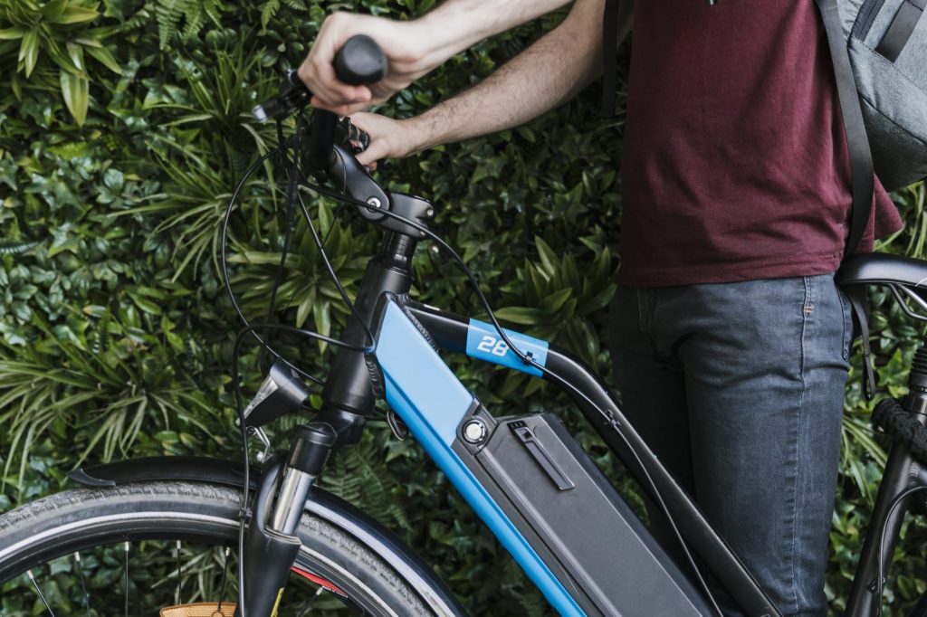 close-up-sideways-cyclist-holding-e-bike-with-green-wall-background