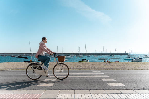 a young woman cycling to work happy on a sunny day with the sea in the background. clear sky with copy space